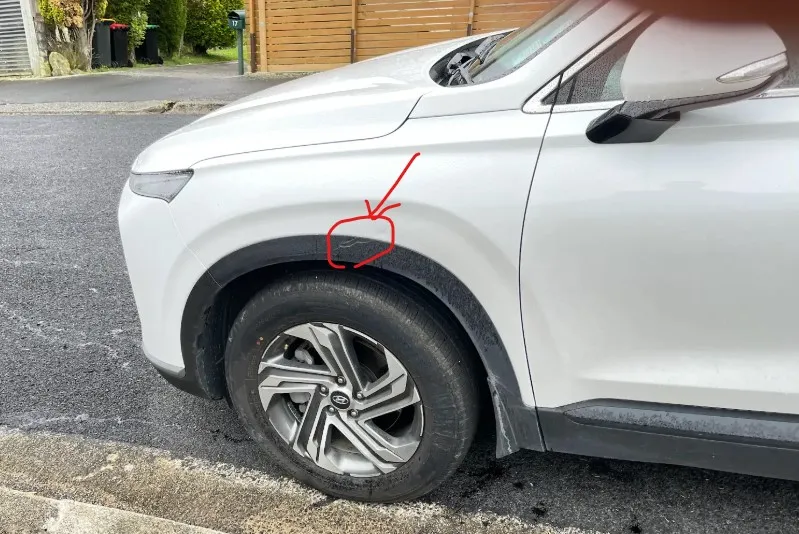 左前輪拱被刮的白色 Hyundai Santa Fe,紅圈標示損傷位置